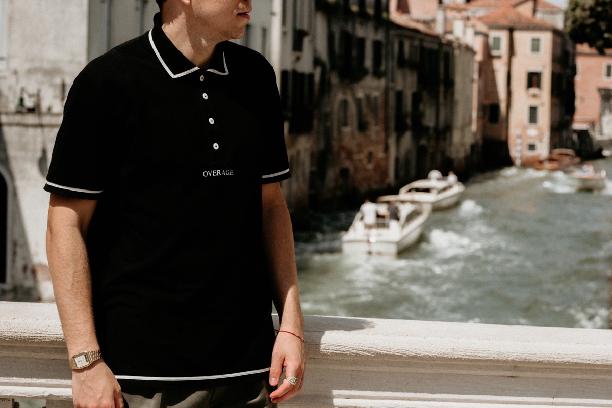 OVERAGE Polo in black, worn on a bridge in Venice